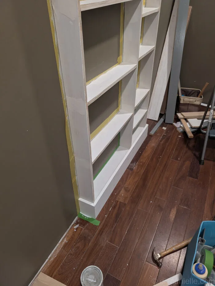 Close-up of shelves with 1x4 top and 1x6 bottom trim boards installed, showing angled mitered corners for a seamless built-in look.
