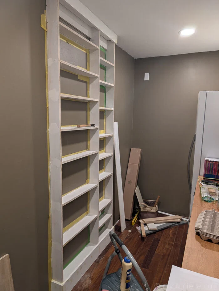 Shelves trimmed with 1x2 boards, showing three vertical pieces and individual trim on each shelf, all attached using a finishing nail gun.
