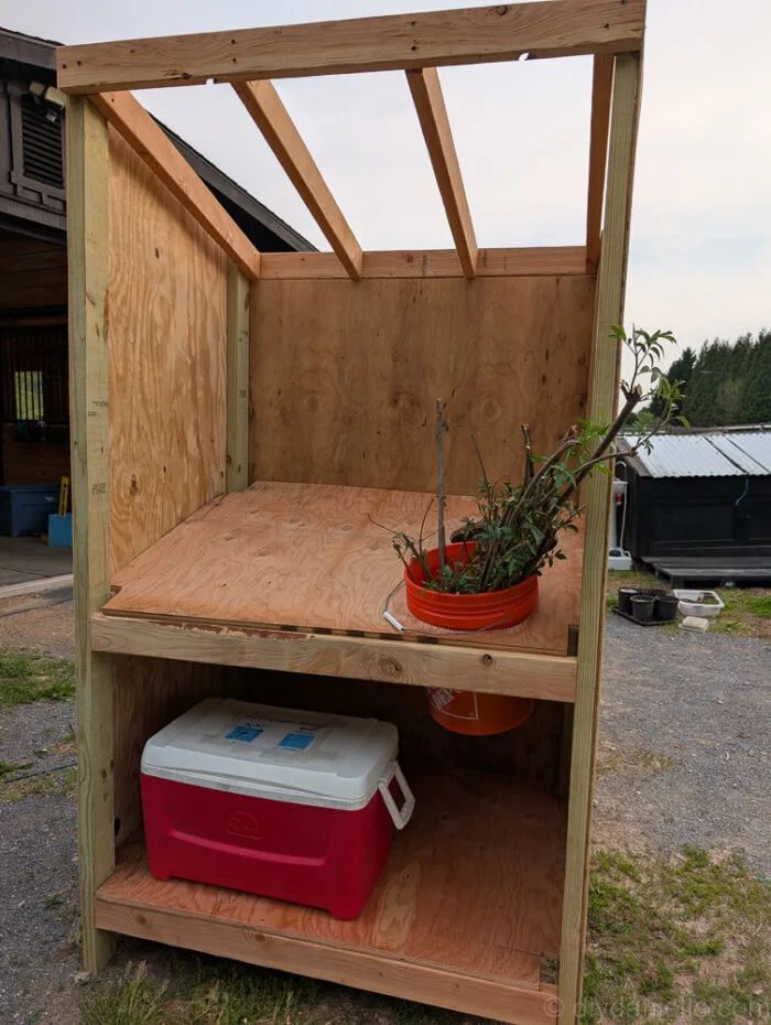 DIY farm stand wood countertop with circular holes cut out for a cooler and 5-gallon buckets.