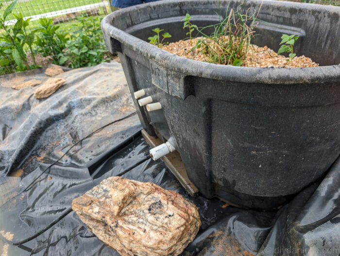 PVC tube entering the front of the bog filter trough from the outside, with a fitting for connecting the pond pump tubing