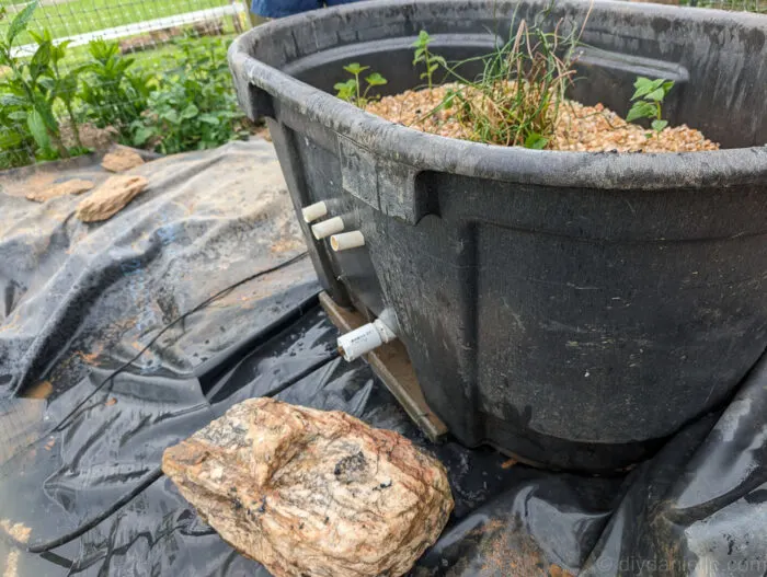 PVC tube entering the front of the bog filter trough from the outside, with a fitting for connecting the pond pump tubing