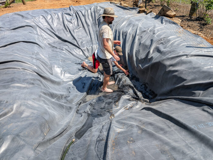 Installing the pond liner, adjusting excess material around edges before filling with water.