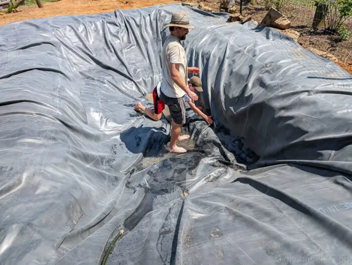 Installing the pond liner, adjusting excess material around edges before filling with water.