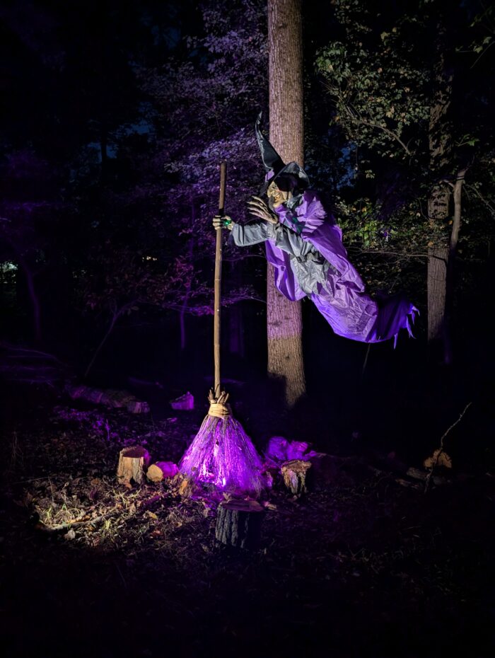 Large floating witch decoration lit with purple lighting along a dark Halloween trail.