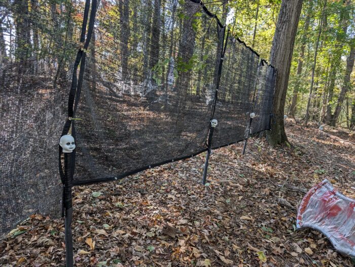 Tall Halloween doll head path markers supporting fabric barriers along a witch-themed outdoor trail.
