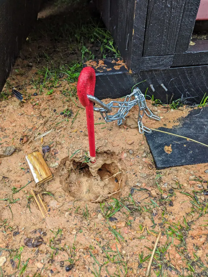 Red metal stake driven into the ground with a chain attached, used to secure a run-in shed area.