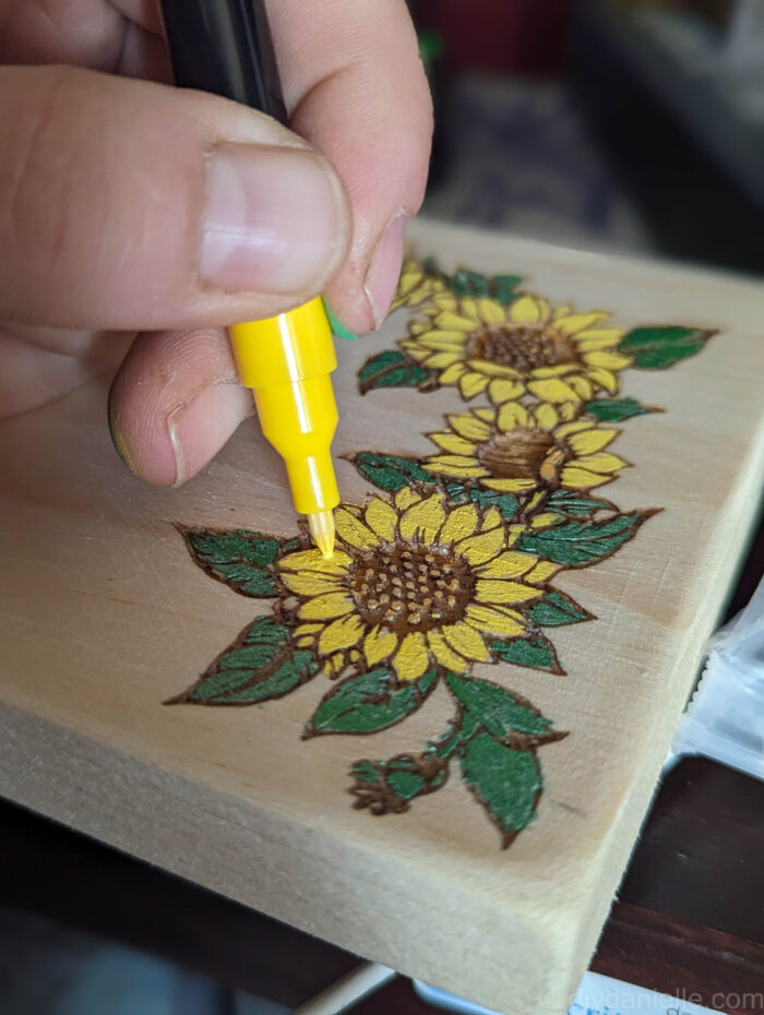 Close-up of a wooden drawer front with a laser-engraved design being filled in with colorful acrylic markers.