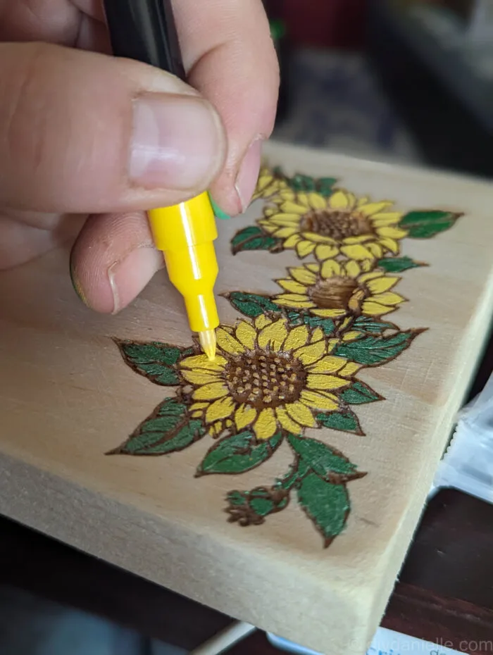 Close-up of a wooden drawer front with a laser-engraved design being filled in with colorful acrylic markers.