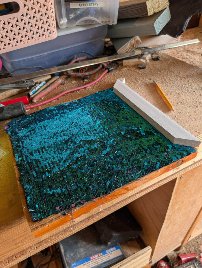 Trim pieces being attached around the edges of a sequin-covered board to frame and finish a DIY fidget board.