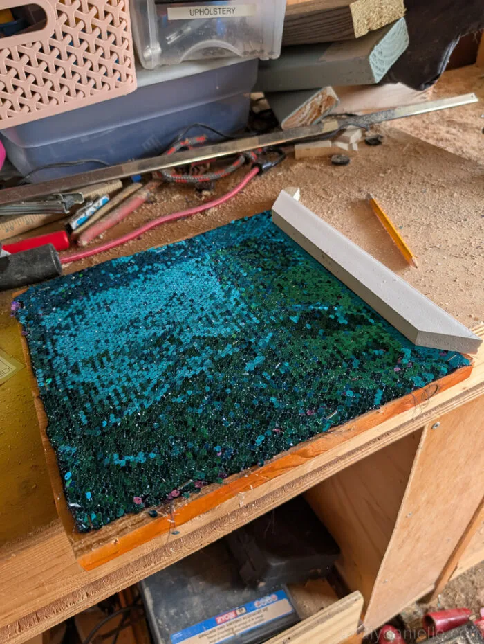 Trim pieces being attached around the edges of a sequin-covered board to frame and finish a DIY fidget board.