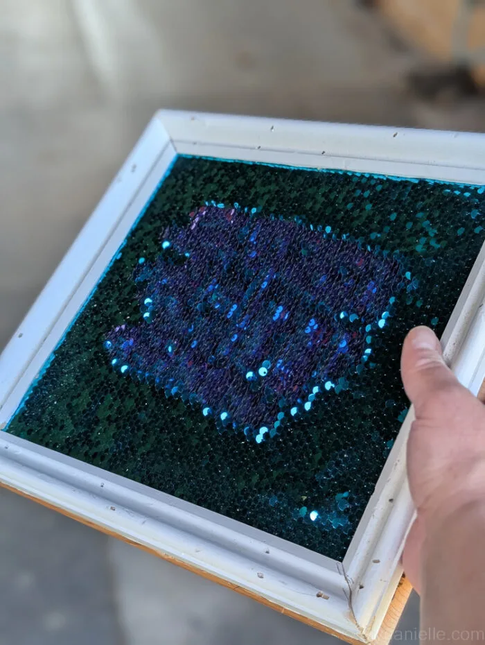 Completed DIY sequin fidget board showing shiny reversible sequins framed neatly on a smooth wooden base.