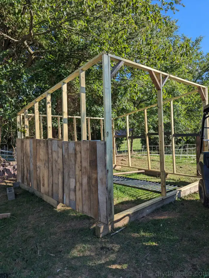 Reclaimed wooden kickboards and siding boards being installed on a DIY run-in shed.