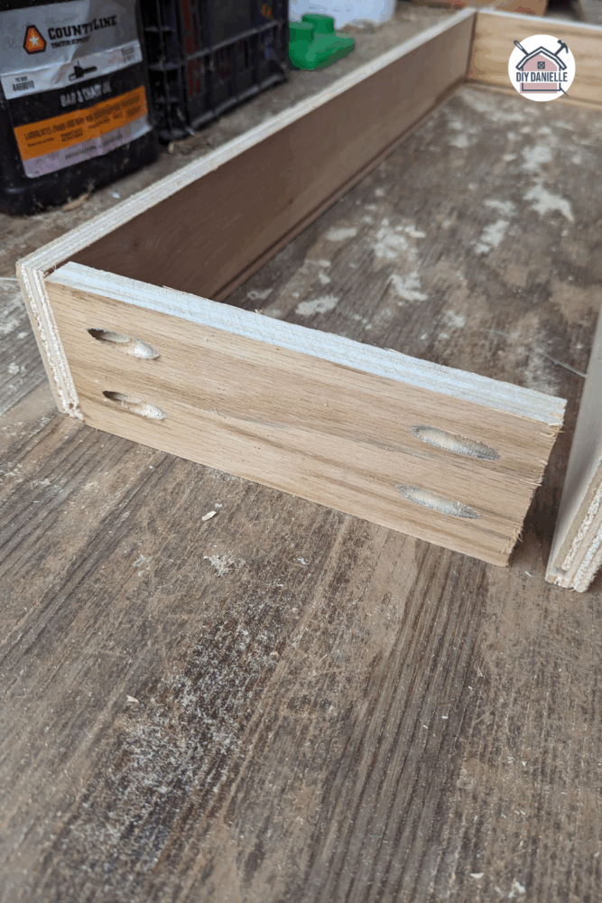 Wooden drawer side panels being attached to a back panel using pocket holes and clamps during DIY drawer assembly.