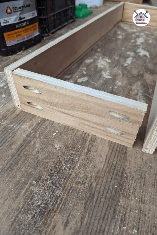 Wooden drawer side panels being attached to a back panel using pocket holes and clamps during DIY drawer assembly.