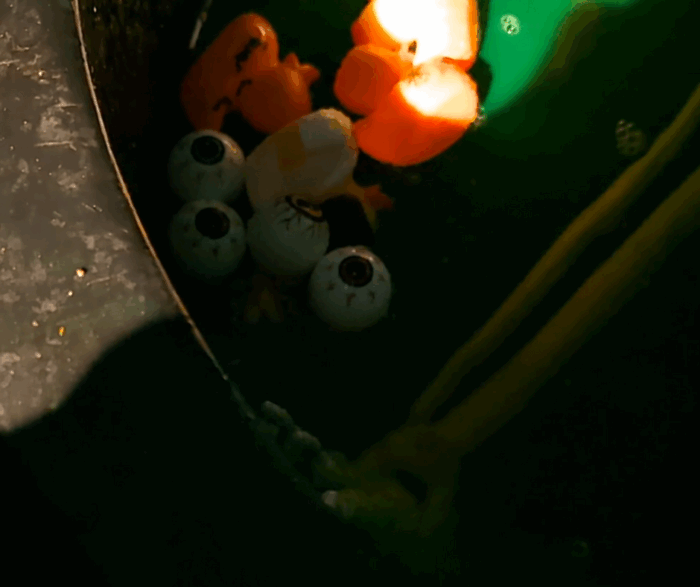 Green bathtub Halloween display with skeleton, floating rubber duckies, and plastic eyeballs.