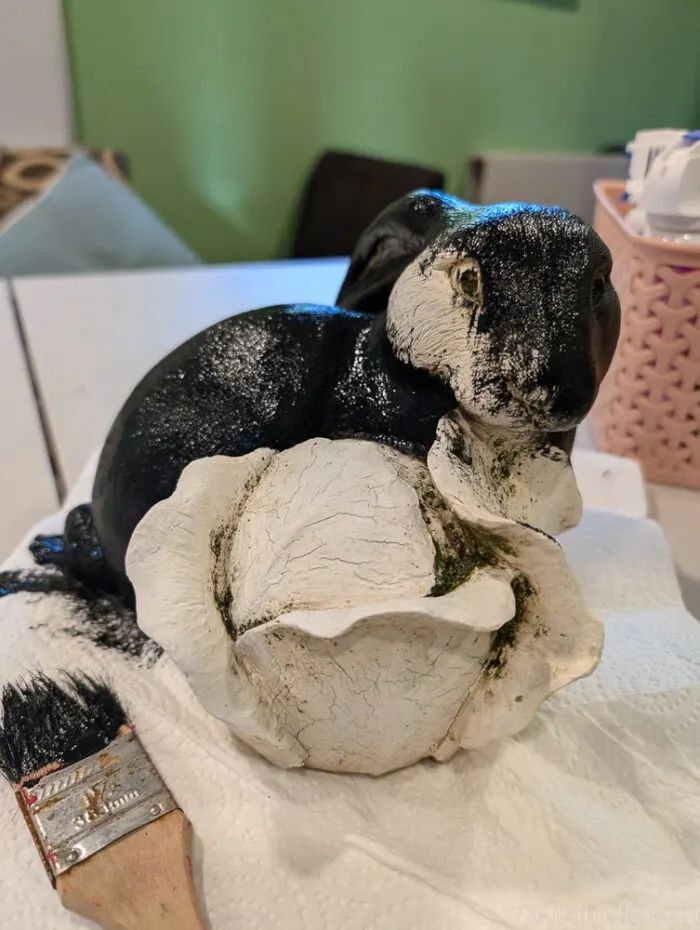 DIY zombie rabbit statue sitting in garden mulch with Halloween props nearby.