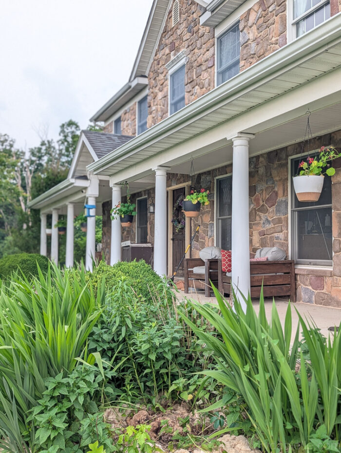 Side view from a distance showing several hanging DIY planters with colorful flowers on a front porch.