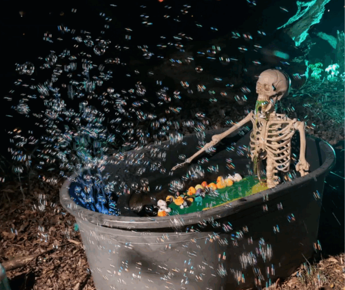 Skeleton sitting in a bathtub filled with green water and overflowing bubbles from a bubble machine.