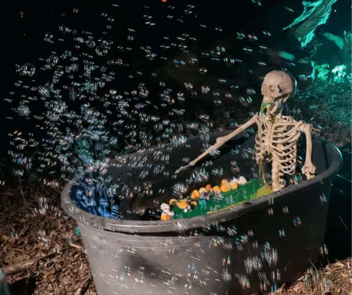 Skeleton sitting in a bathtub filled with green water and overflowing bubbles from a bubble machine.