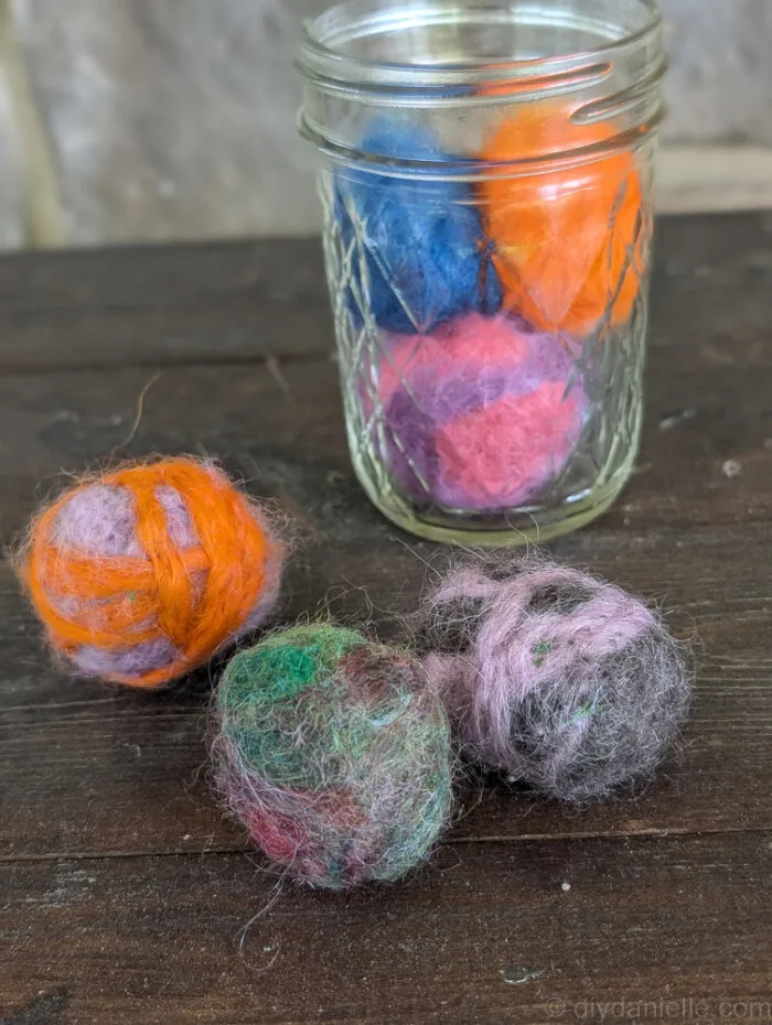 Container filled with homemade needle felted catnip balls ready for storage and play