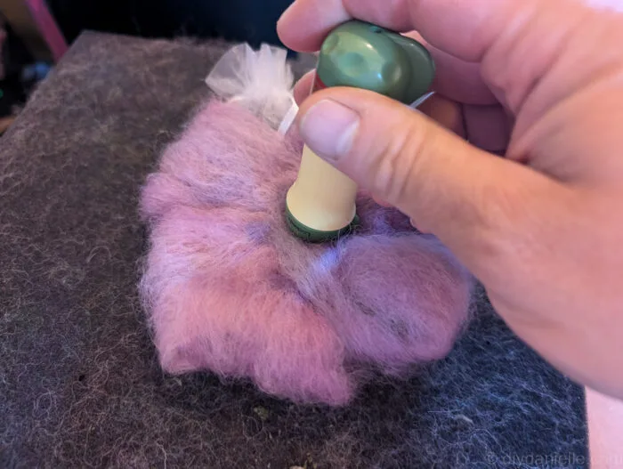 Felting needle poking through wool with small bells embedded, showing careful needle felting technique