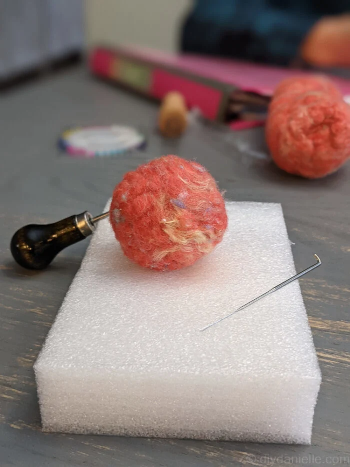 Needle felting wool into a round shape while lifting it off the foam pad to avoid sticking