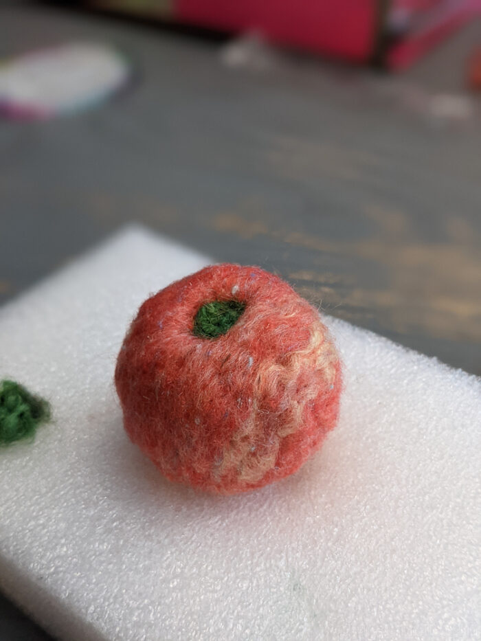 Needle felted wool ball with green wool added on top to resemble an apple or decorative detail
