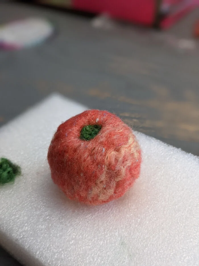 Needle felted wool ball with green wool added on top to resemble an apple or decorative detail