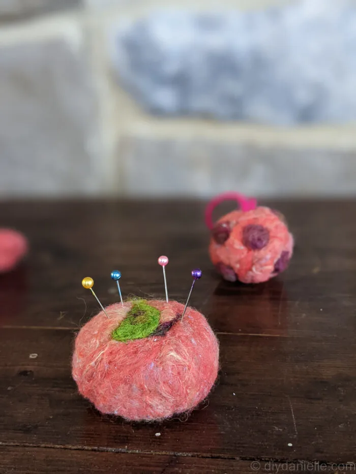 Needle felted apple-shaped ball repurposed as a pin cushion with a magnet inside