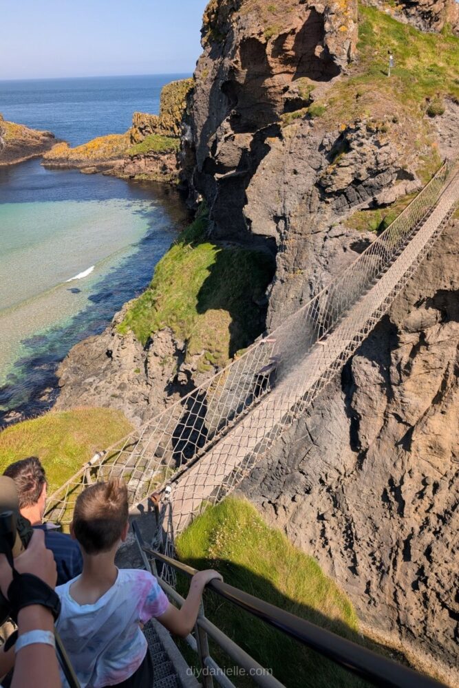 People walking across the Carrick-a-Rede rope bridge with cliffs and ocean in the background, Northern Ireland.
