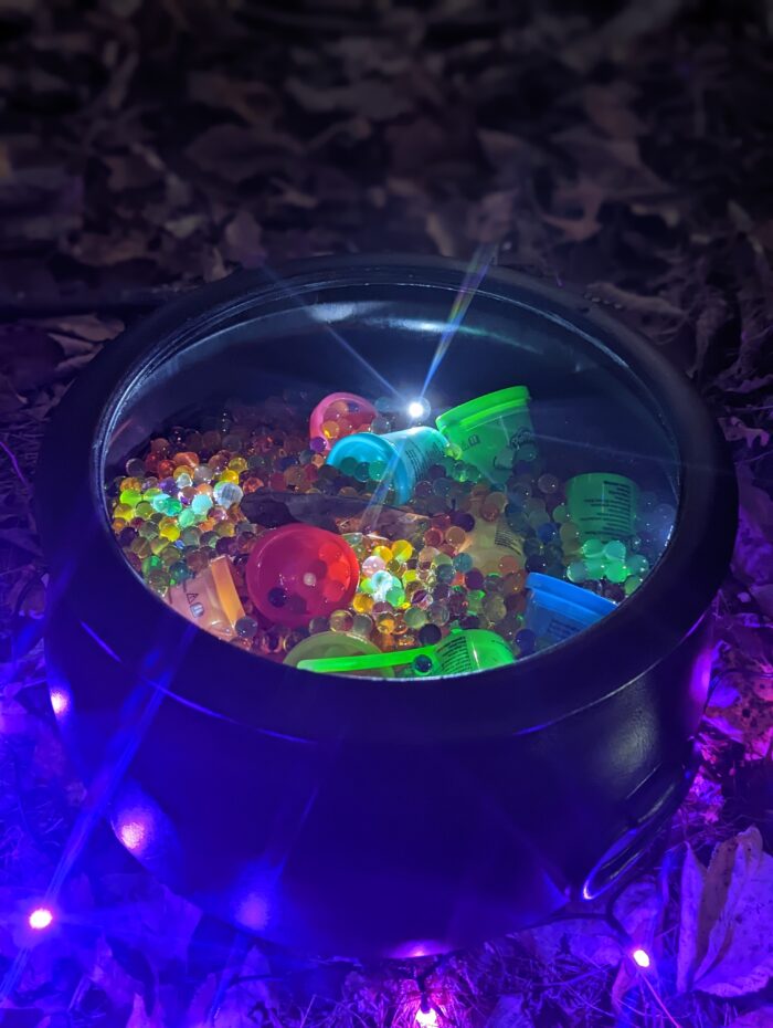 Black cauldron filled with water beads and non-food treats set up as a Halloween trick or treat station along a decorated trail.