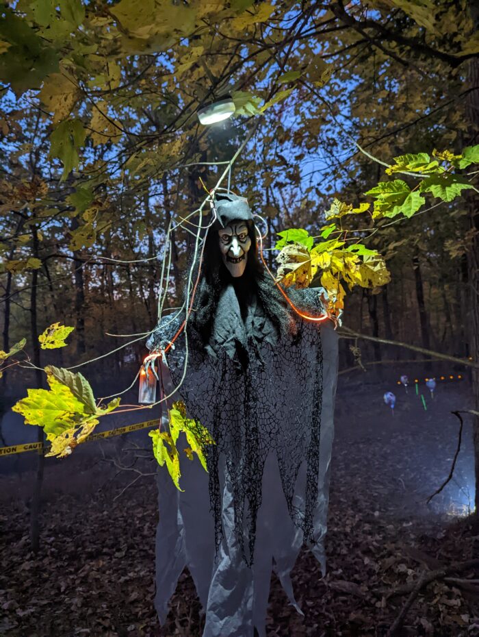 Halloween yard decorated with witch props lit up by spotlights, making decorations visible in the dark