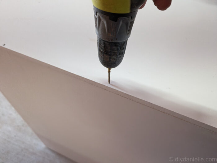 Close-up of trim head screws and adhesive being used to secure PVC panels for a DIY ball python enclosure, showing recommended screw lengths.