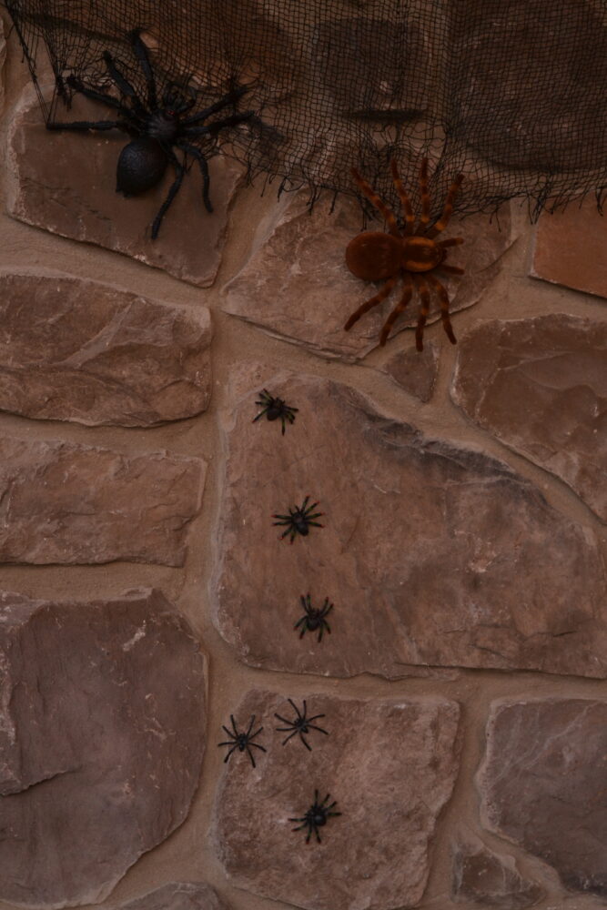 Spider webs and Halloween spider decorations attached to stone porch walls using hot glue for a secure, damage-free setup.