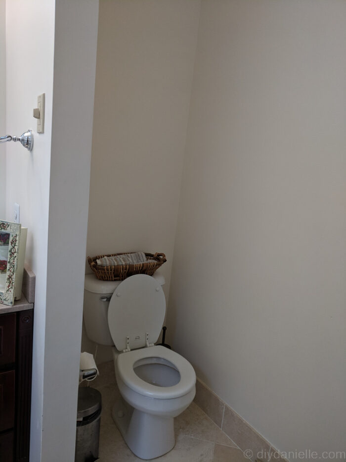 Bare space above a toilet before installing DIY over-the-toilet storage shelves.