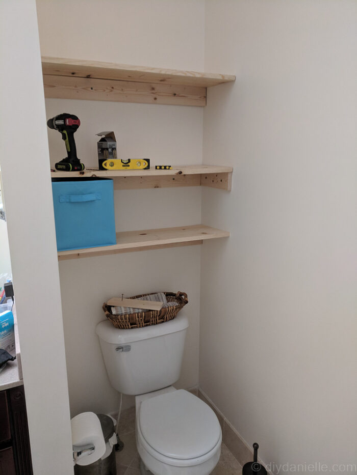 Unfinished DIY over-the-toilet shelves showcasing natural wood beauty before any additional finishes or drawer installation.