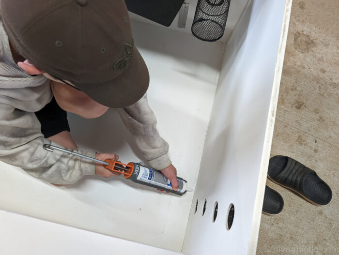 Applying caulk to the interior edges of a DIY ball python enclosure to ensure a secure, leak-proof habitat for reptiles.
