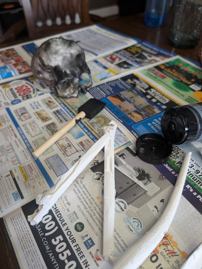 Skull pieces for a DIY baby mobile being painted with red and black acrylic paint on a work surface.