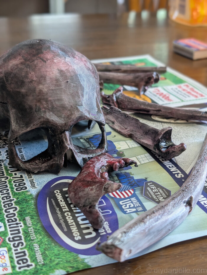 Painted skull pieces for a DIY baby mobile laid out on newspaper to dry.