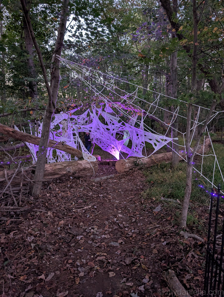 Spooky hanging corpse in webbing with a trio of purple-glowing spider egg sacs for Halloween décor.