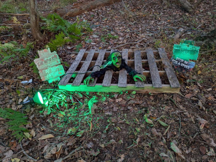 Zombie animatronic crawling on a pallet with green light shining from underneath for a spooky Halloween effect.