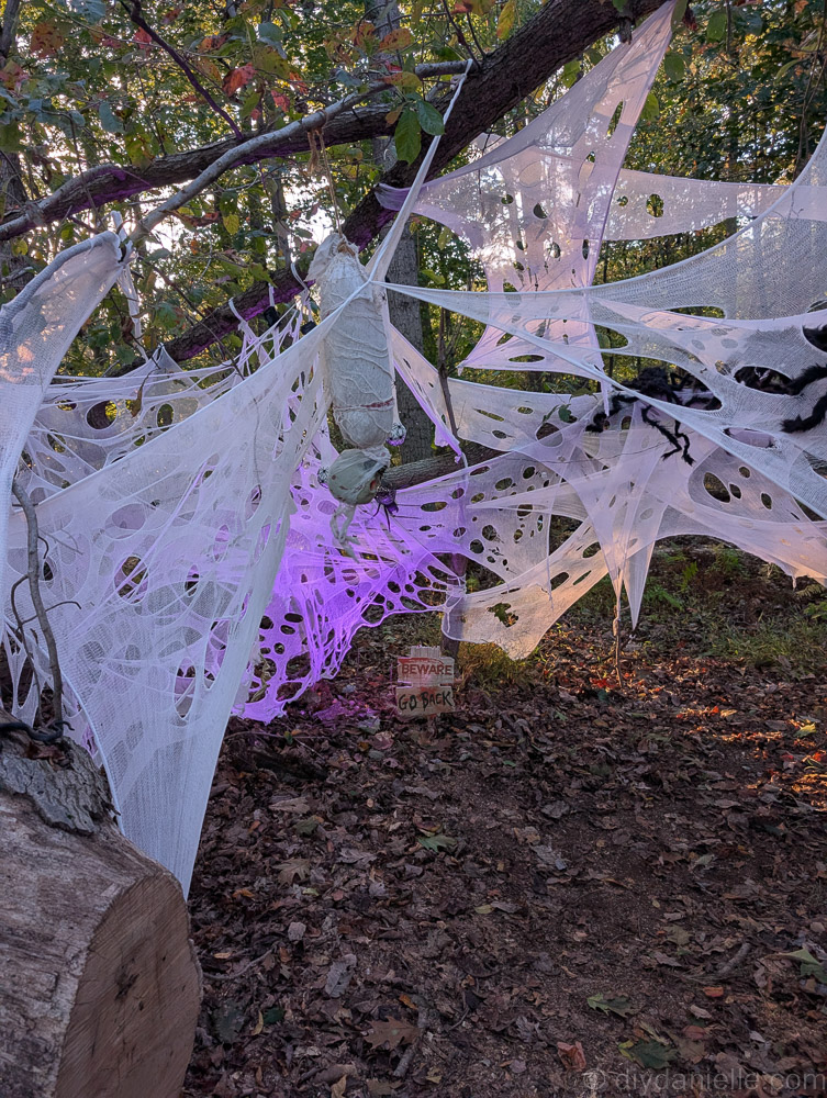 Creepy Halloween display featuring a suspended corpse and three glowing purple spider egg sacs.