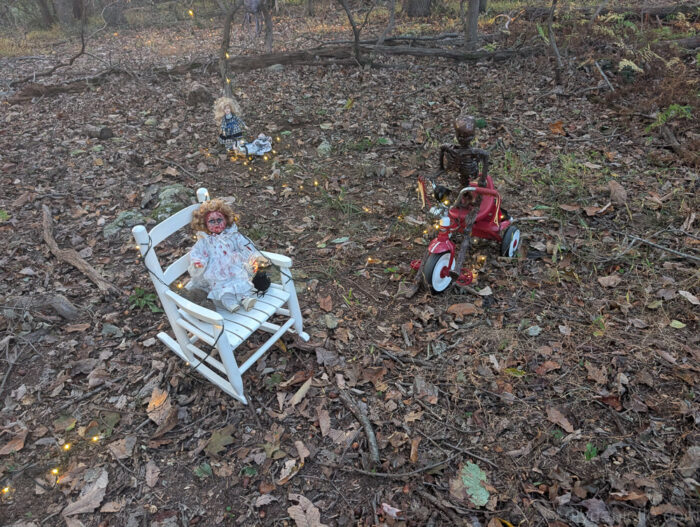 Halloween display of a skeleton riding a tricycle with a baby doll sitting in the back cubby.