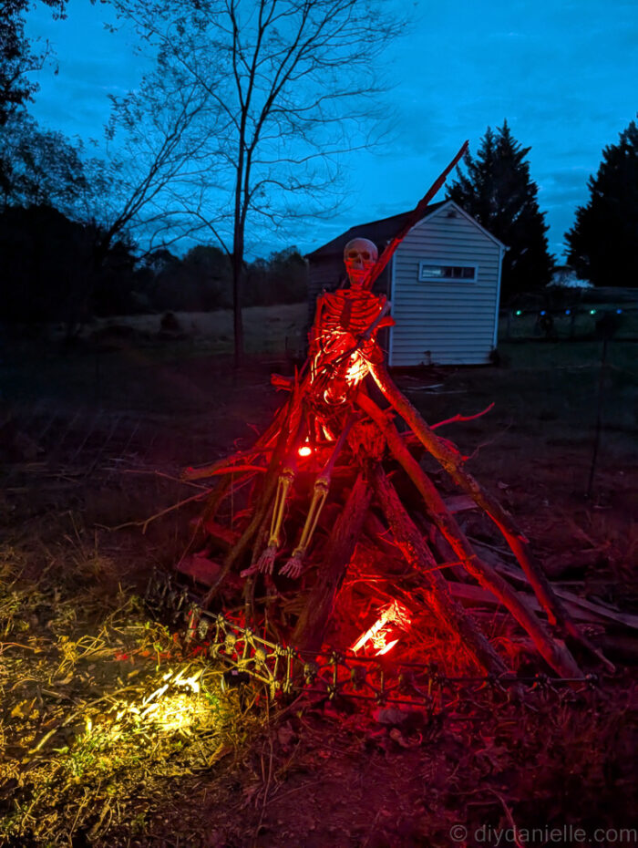 Halloween display with a skeleton on a pyre next to an axe, lit with red lights to create the effect of a witch on fire.