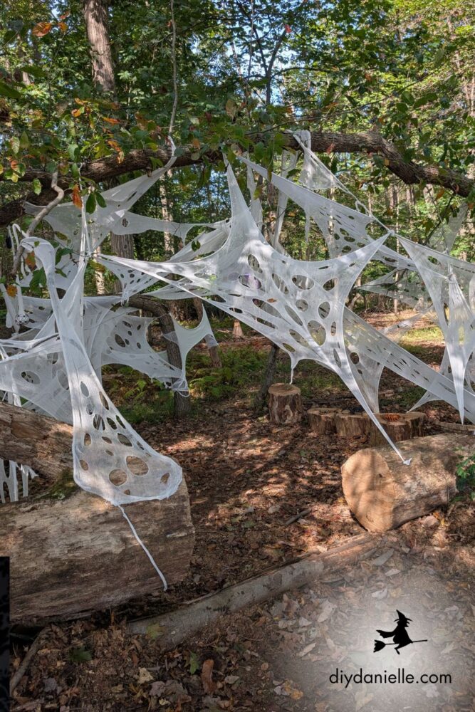 Spider web tunnel made with beef netting stretched between tree trunks for an outdoor Halloween decoration