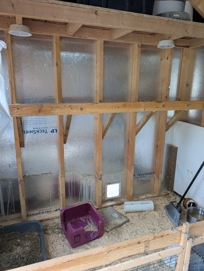 2x4 wood board being attached across the top front of a wall mounted hay feeder, screwed into wall studs for support.