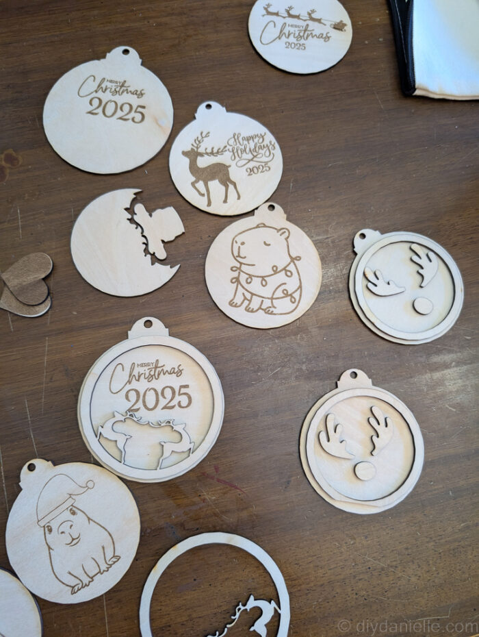 Two-layer wooden Christmas ornament pieces arranged on a sheet of wood, freshly cut by a laser cutter and ready to be removed for assembly.
