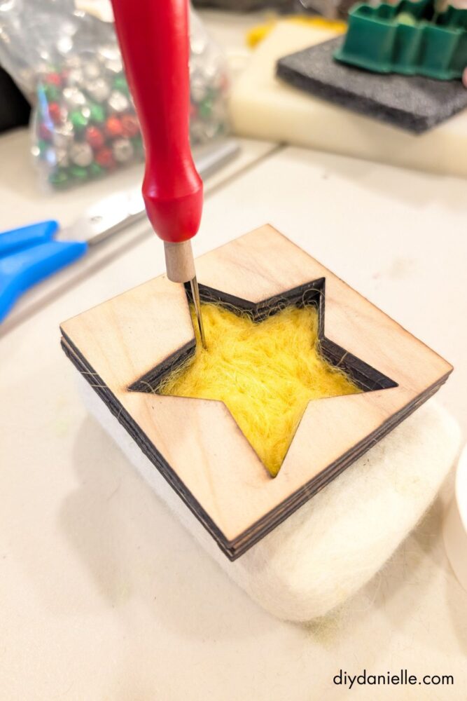Close-up of a felting needle shaping wool roving inside a cookie cutter, showing the needle-felting process for DIY ornaments.