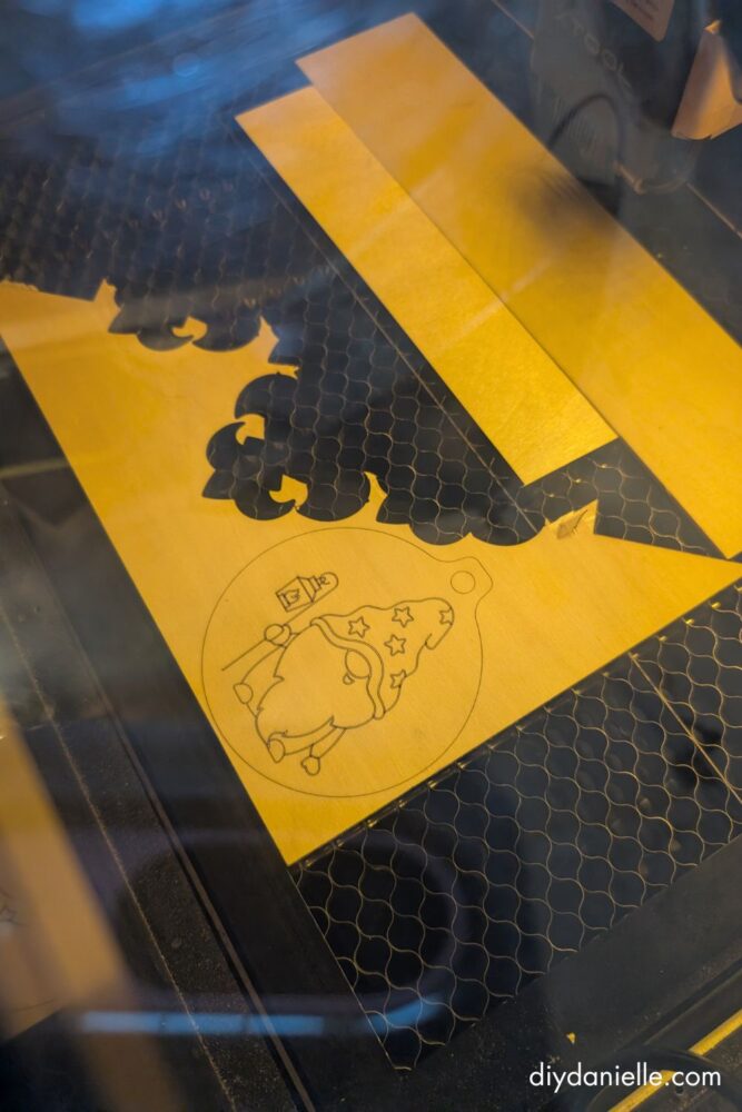 Close-up of a DIY crafting machine in use with a warning to monitor it for safety during ornament making.