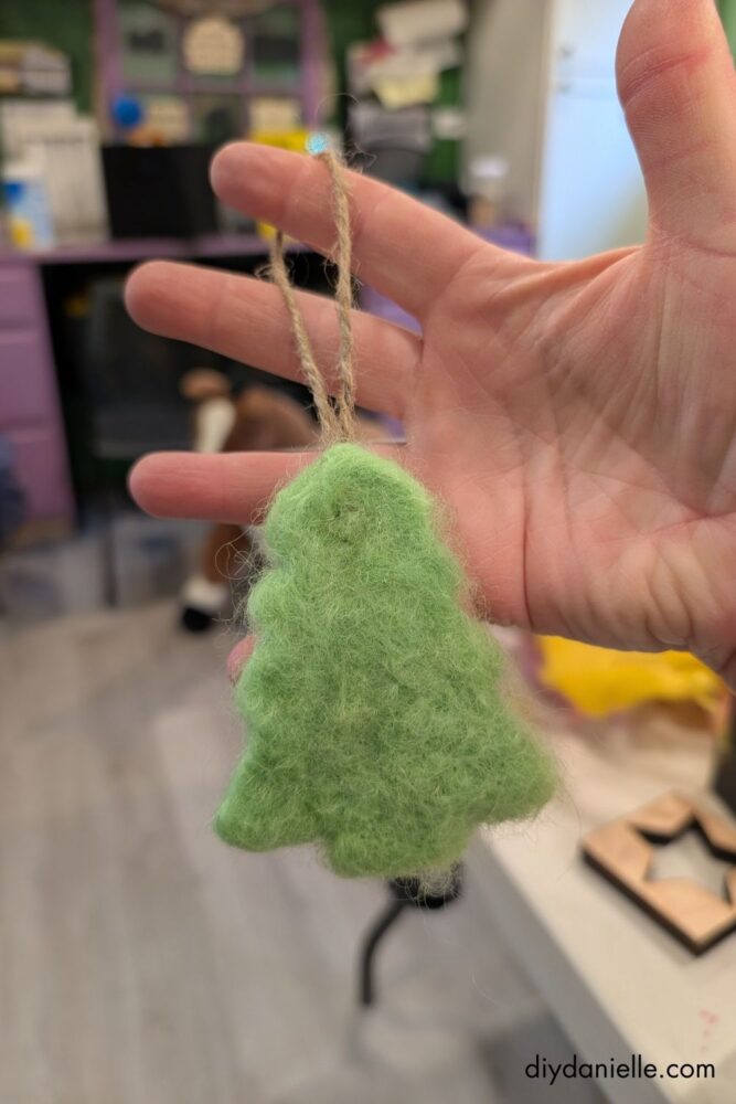 Hands lifting a partially felted wool ornament from a felting pad while shaping it with a cookie cutter for a DIY needle-felting project.